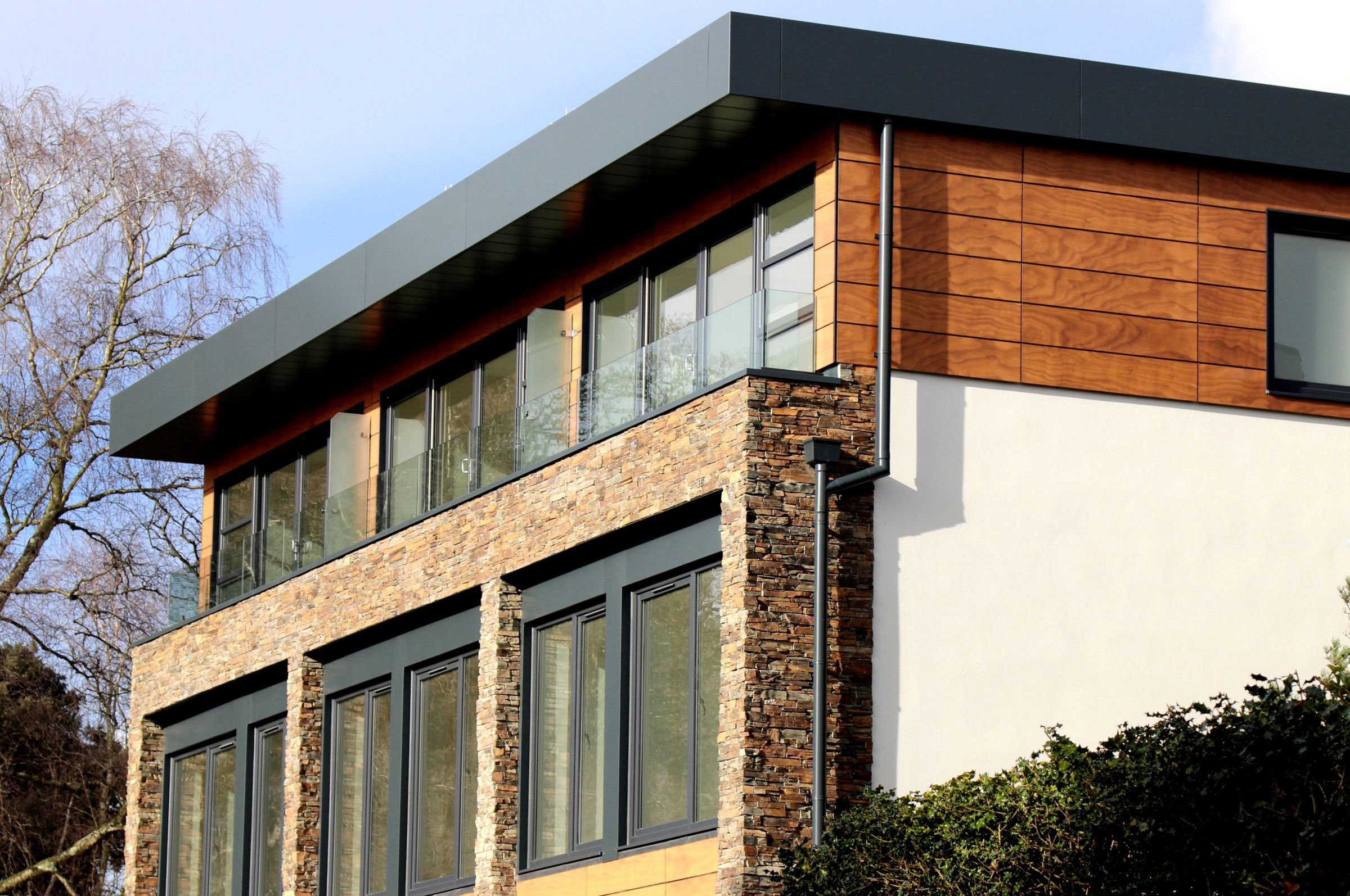 Moderne Fassade mit Holzverkleidung, Naturstein und großen Fenstern.