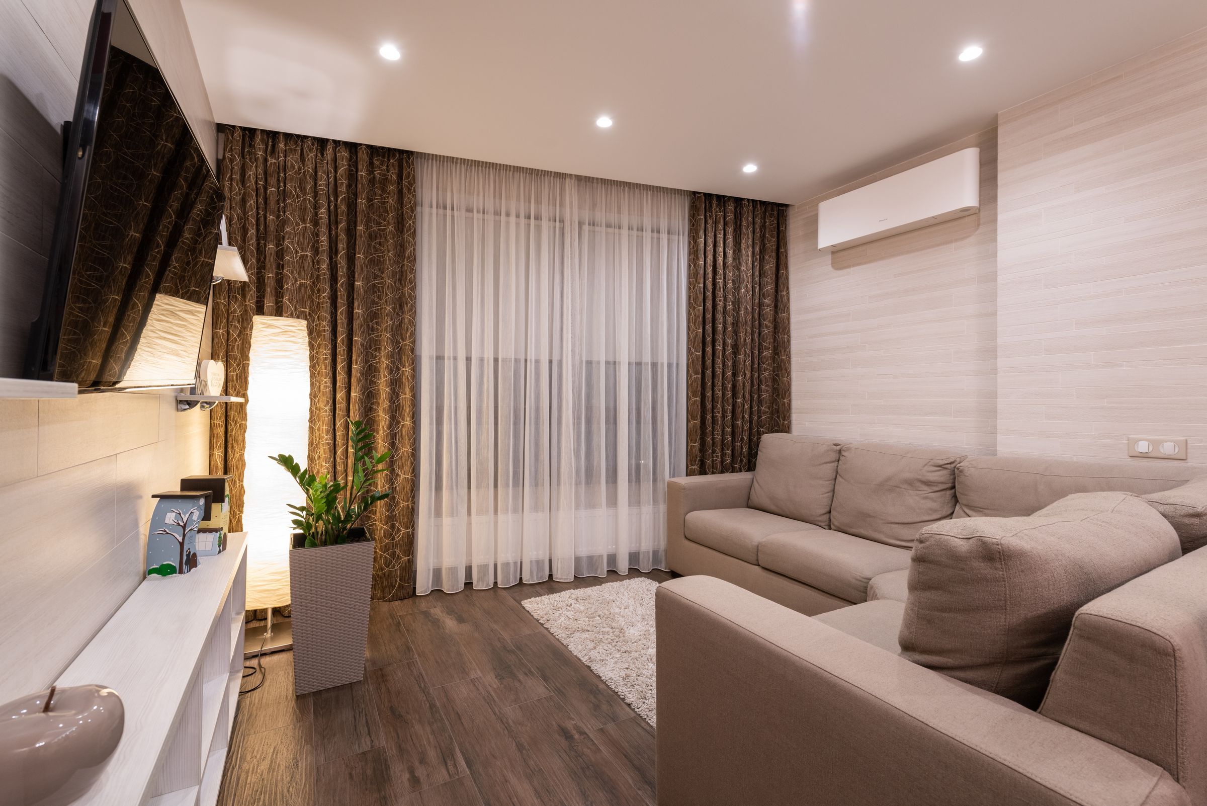 Wohnzimmer mit beigem Ecksofa, Stehleuchte, Wandleuchte und Deckenspots.