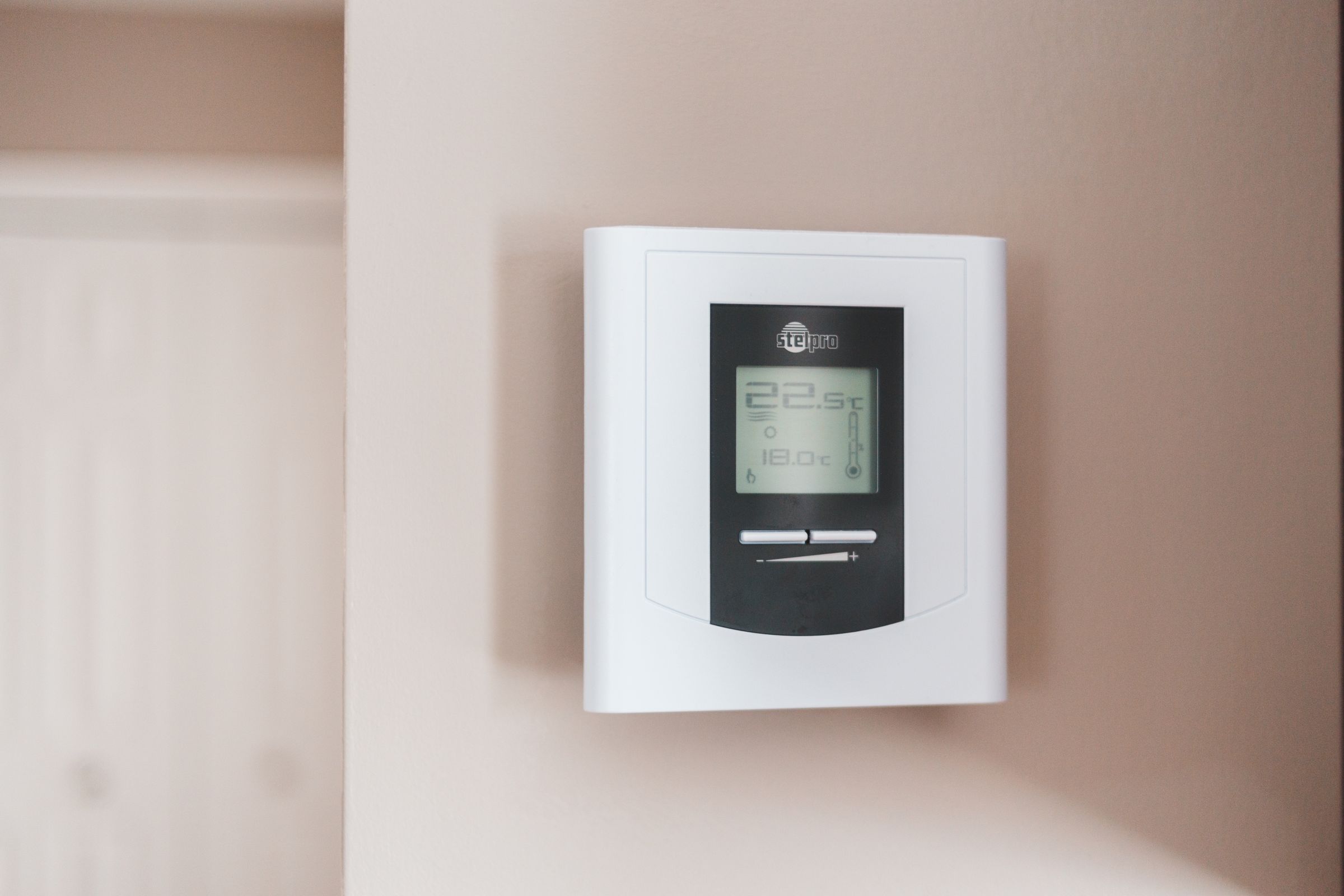 Digitales Wandthermostat mit Temperaturanzeige an einer hellen Wand.